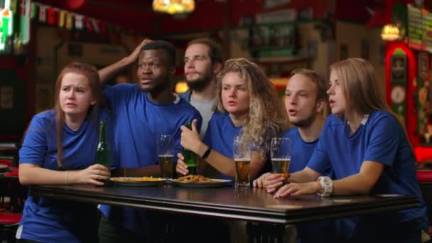 Een groep vrienden van fans in blauwe t-shirts opgewonden emotioneel kijken naar de wedstrijd en verheugen op het doel gescoord, springen en schreeuwen emotioneel. Vier en vier een goal gescoord door te kauwen met bier - Video