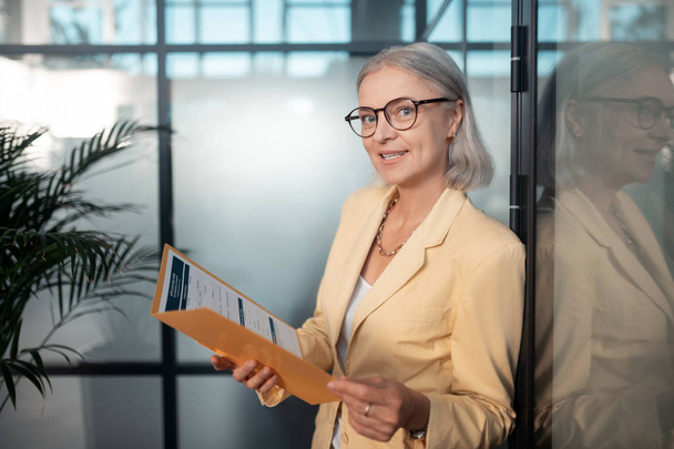 Pleased businesswoman in eyeglasses holding a paper folder - 写真・画像