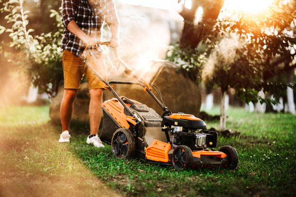 Gardener using industrial lawnmower during summer sunset. Close up details of landscaping and gardening.  - 写真・画像