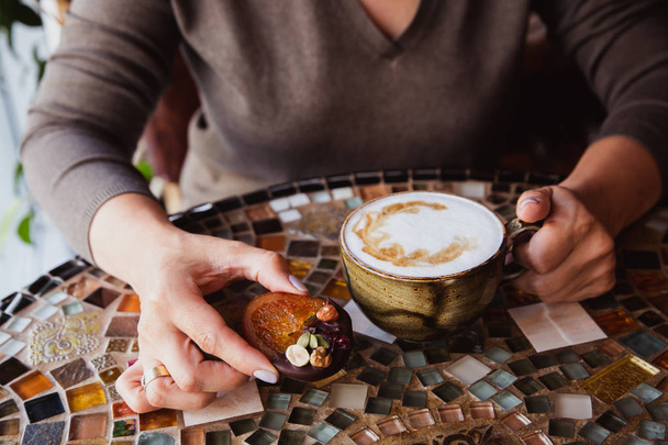 Las manos de mujer sostienen una taza de café capuchino en una mesa de vidrio de color en la cafetería - Foto, imagen