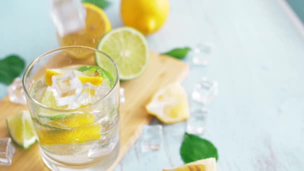 スライスライムとレモンで氷が落ちるイントロガラスのスローモーションをクローズアップ。新鮮なコクテールは、まな板に滞在します。夏の飲み物. - 映像、動画