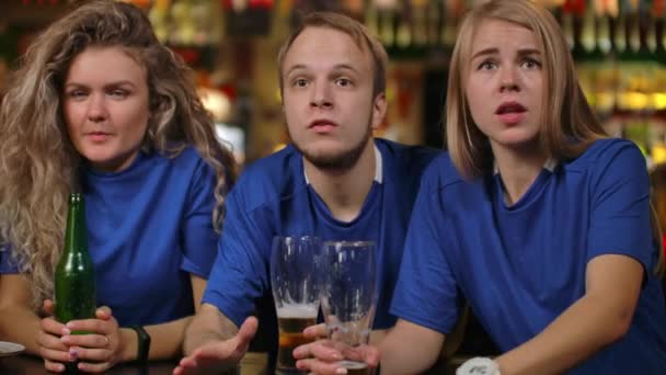 Close-up groep van fans emotioneel kijken naar een sport uitgezonden in een bar op TV met bier, mannen en vrouwen in blauwe T-shirts van verschillende rassen, zijn boos na het verliezen en verliezen van hun team - Video