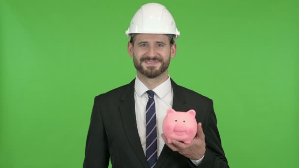 fröhlicher Ingenieur zeigt auf Sparschwein gegen Chromschlüssel - Filmmaterial, Video
