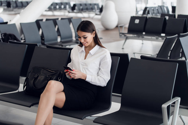 Женщина читает телефонные сообщения в зале ожидания аэропорта. Happy girl buying e-ticket, making hotel reservations and check in online
. - Фото, изображение