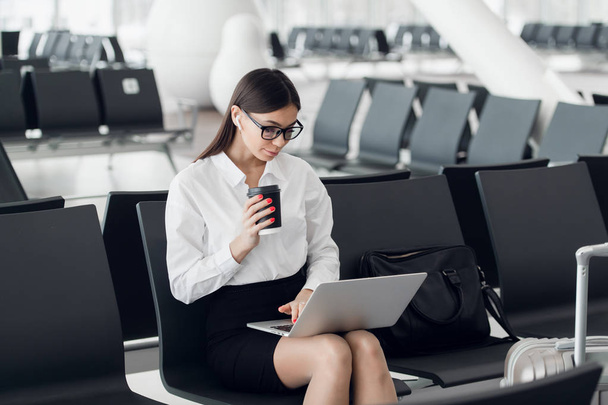 Молода жінка з кавою, що працює на ноутбуці, сидить у від'їзді аеропорту
 - Фото, зображення