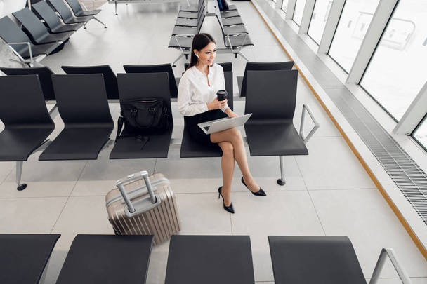 Молодая женщина, работающая на ноутбуке, сидит в зале вылета аэропорта
 - Фото, изображение