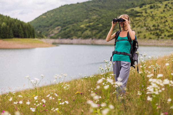 Woman hiker using binoculars while spending time in the beautiful nature. - 写真・画像