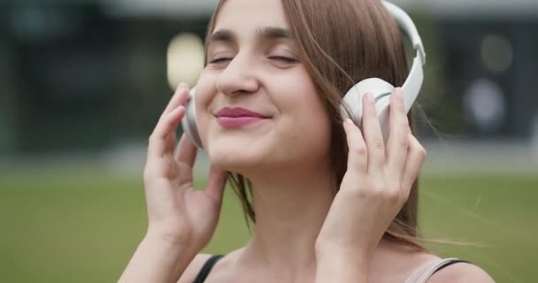 Happy young woman enjoying music dancing in the street. Joyful young woman listening to music wear earphone at urban background - Séquence, vidéo