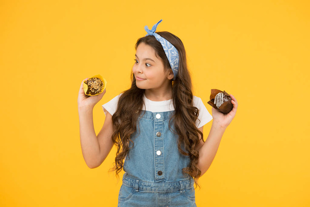 Delicious cupcakes. Happy childhood. Adorable smiling child with cupcakes on yellow background. Cafe restaurant food. Yummy cupcakes. Bakery and confectionery concept. Kid girl hold glazed muffins - Fotoğraf, Görsel