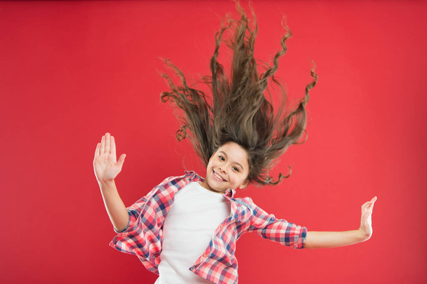 Amazing long hair. Cute small girl with long hair curls waving on red background. Adorable little child taking care of long brunette hair. Enjoying long curly hairstyle - Zdjęcie, obraz
