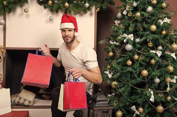 The morning before Xmas. man in santa hat hold christmas present. online christmas shopping. New year scene with tree and gifts. happy santa man. delivery christmas gifts. Winter holidays sales - Foto, immagini