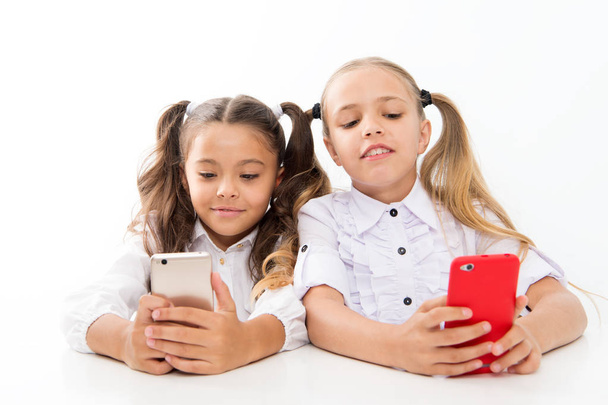 Σύγχρονοι μαθητές. Μικροί μαθητές που χρησιμοποιούν κινητά τηλέφωνα σε τάξη απομονώνονται σε λευκό. Οι μικροί μαθητές στέλνουν μηνύματα στο μάθημα. Χαριτωμένο μαθητές λυκείου κατάδυση βαθιά σε μαθήματα smartphone - Φωτογραφία, εικόνα