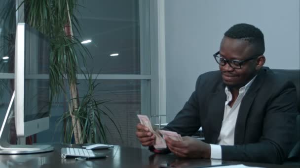 Afro businessman counting cash, sitting at desk in office - Imágenes, Vídeo