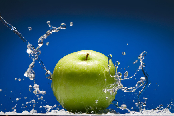 Green apple with water splash on blue background - 写真・画像
