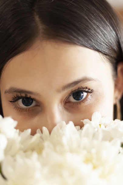 Attractive middle-eastern girl with beautiful eyes looking into the camera from behind flowers bouquet - Fotoğraf, Görsel