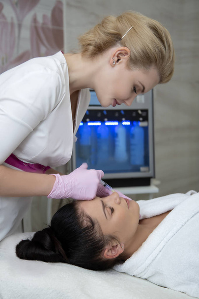 A beautician with blond hair is doing a procedure for increasing the lips of a brunette - Zdjęcie, obraz