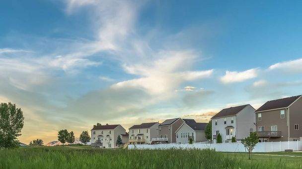 Panorama Terreno expansivo coberto com gramíneas verdes ricas na frente de casas de família
 - Foto, Imagem