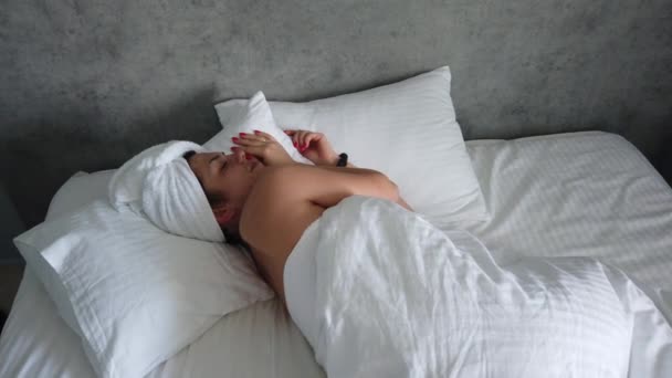 Beautiful young girl is sleeping on a white pillow. She is waking up, stretching and smiling. Handheld real time medium shot - Materiał filmowy, wideo
