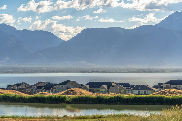 Otthonok közepette csillogó tó, kilátással a távoli hegyi fölé magasodó völgyben - Fotó, kép
