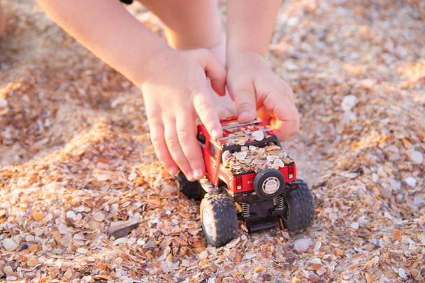 close up of little boy playing with toy car on at beach, summer vacation concept - Photo, Image