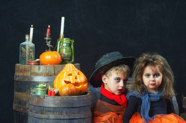 Irmão e irmã no Halloween, crianças em trajes de carnaval contra uma parede escura. Crianças, abóboras e velas. Há espaço para texto
 - Foto, Imagem