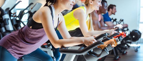 Asian woman and her friends on fitness bike in gym - Photo, Image