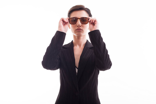 Beautiful young model posing with sunglasses and wearing a black jacket over white background in studio - Fotoğraf, Görsel