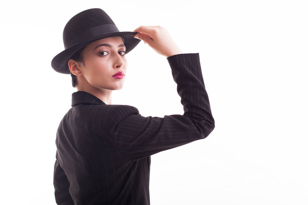 スタジオで白い背景の上にスタイリッシュな黒い帽子を持つ美しい若いモデル - 写真・画像