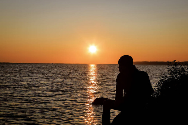 un gars est assis sur une montagne au lever du soleil sur fond d'une énorme rivière
 - Photo, image