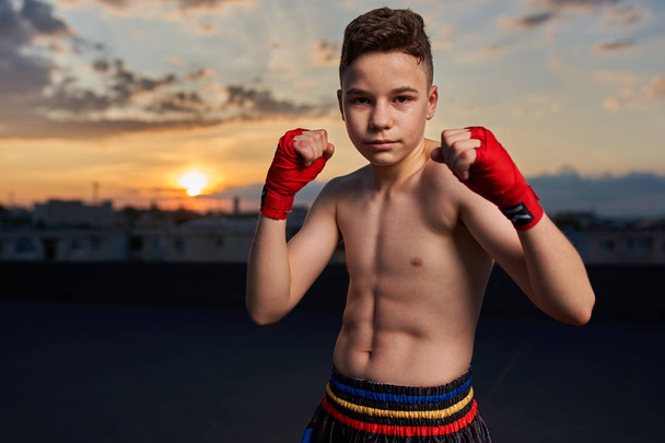 Young kickboxer training on the roof at sunset - Foto, Bild