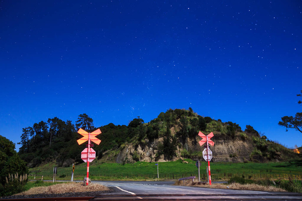 Przejazd kolejowy w Nowej Zelandii wsi, sfotografowany w nocy pod gwiaździste niebo. Południowy krzyż jest widoczny na środku po prawej stronie zdjęcia - Zdjęcie, obraz