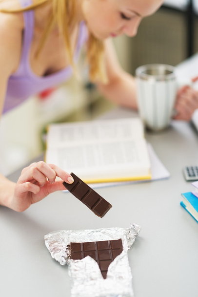 Closeup on teenager girl eating chocolate while studying in kitc - Foto, afbeelding