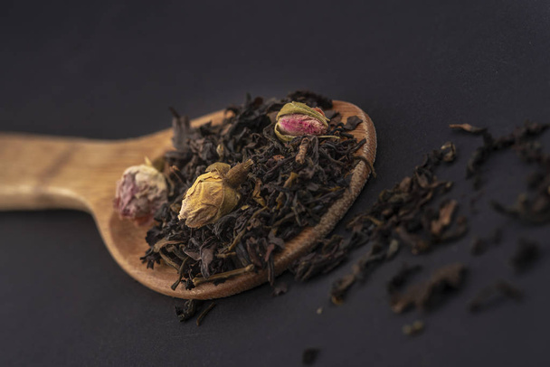 aromatic black dry tea with rose flowers on a wooden spoon isolated on black background - Photo, image