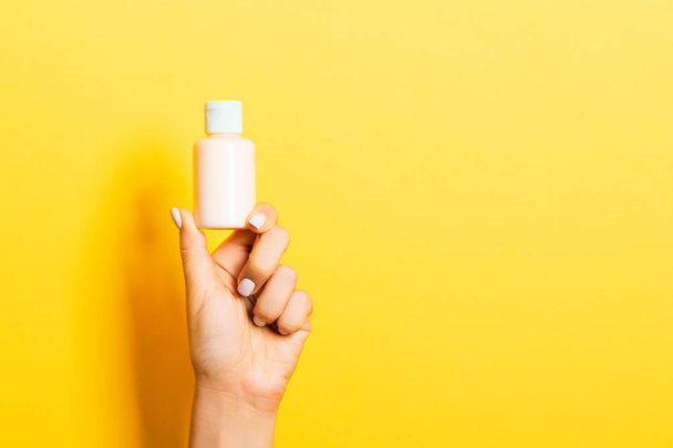 Botella de crema de mano femenina de loción aislada. Chica dar productos cosméticos tarro sobre fondo amarillo
 - Foto, imagen