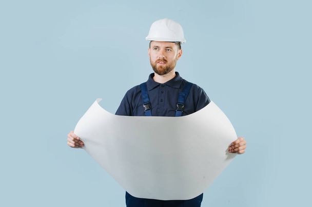 Construction engineer in a white helmet and blue uniform with a paper schematics - Foto, Imagen