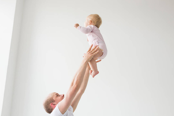 Feliz padre joven levantando lindo bebé en alto en el aire, pasar y disfrutar del tiempo junto con su hija
 - Foto, Imagen