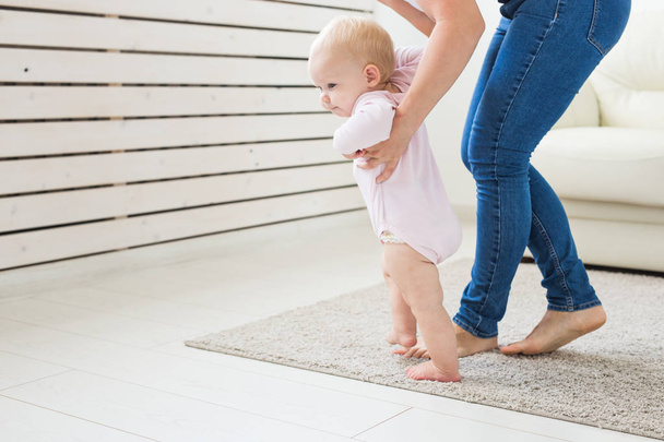 Primeros pasos del bebé pequeño aprendiendo a caminar en la sala de estar soleada blanca. Calzado para niños
. - Foto, imagen