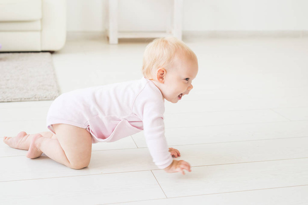 Childhood, children and babyhood concept - crawling funny baby girl indoors at home - 写真・画像