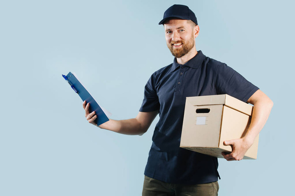 Delivery man in uniform is checking his orders list while holding box under arm - Foto, imagen