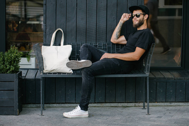 Young man holding white textile eco bag against urban city background. . Ecology or environment protection concept. White eco bag for mock up. - Fotó, kép