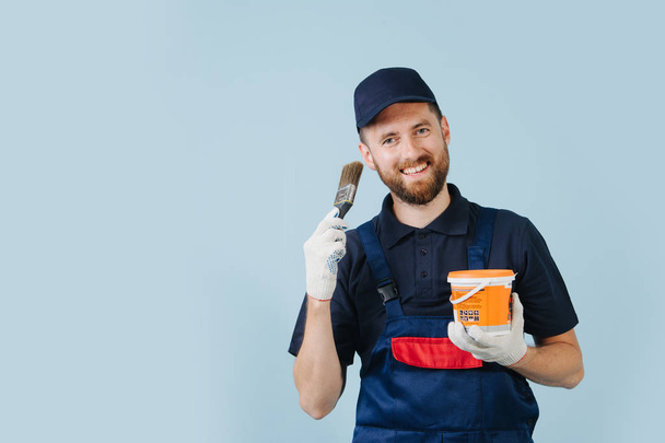 Cheerful service worker with paint can and brush in hands dressed in uniform - Foto, Imagen