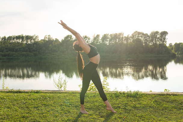 Mujer joven disfrutando de yoga relajante al aire libre en el parque
. - Foto, Imagen