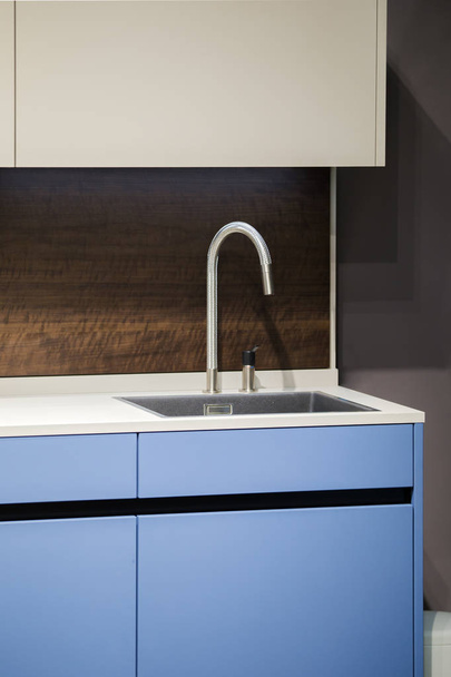 Beautiful blue kitchen unit, kitchen faucet, wooden apron in the kitchen. Modern minimalistic kitchen design - 写真・画像