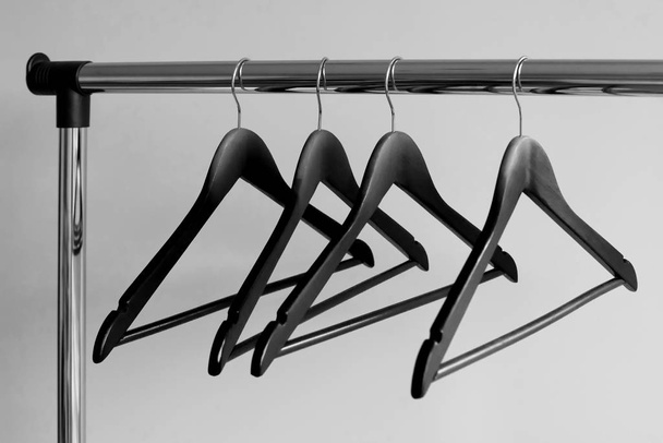 Leere Kleiderbügel auf Metallschienen vor grauem Hintergrund. rechteckige Kleiderstange aus Metall mit leeren schwarzen Kleiderbügeln aus Holz. - Foto, Bild