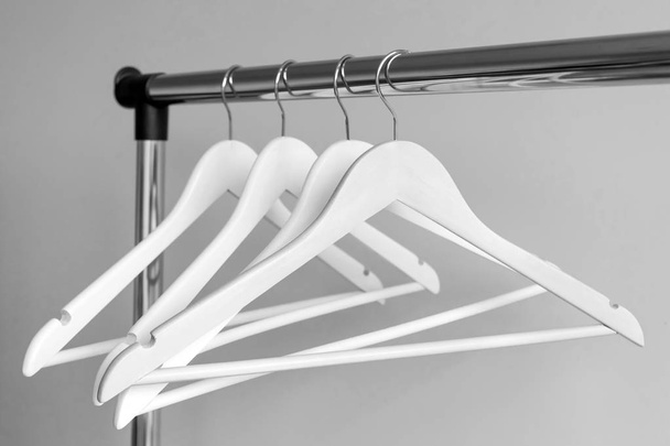 Leere Kleiderbügel auf Metallschienen vor grauem Hintergrund. rechteckige Kleiderstange aus Metall mit leeren weißen Kleiderbügeln aus Holz. - Foto, Bild