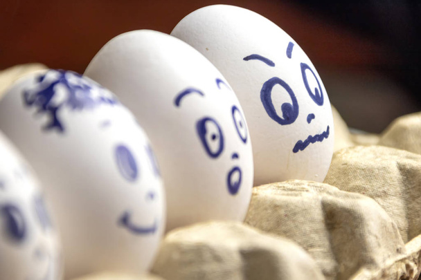 Lovely eggs in cardboard box. Eggs with emotions. White eggs in cardboard box with different faces painted on them. Boys and girl - Foto, Imagen