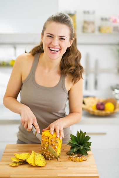 Smiling young woman cutting pineapple - Фото, изображение