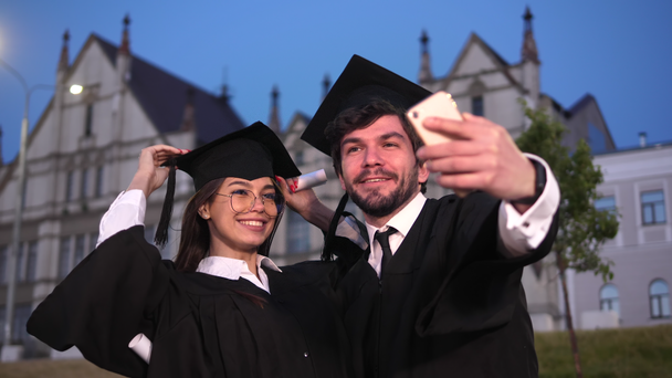 Studenti laureati di sesso maschile e femminile che si fanno un selfie con il cellulare. Coppia emotiva. - Filmati, video