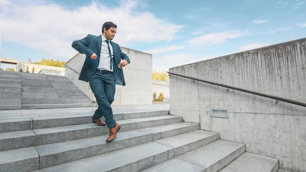 スーツを着た陽気で幸せなビジネスマンは、階段を歩きながらコーヒーを飲みながら積極的に踊っています。ビジネスセンターの隣にある都市コンクリート公園で撮影されたシーン。晴れた. - 写真・画像