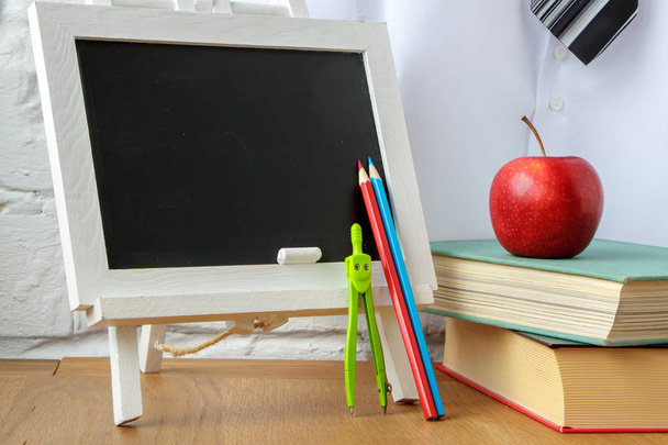 Material escolar, placa de giz em miniatura, uma pilha de livros e uma maçã na mesa, foco suave
 - Foto, Imagem